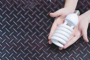 energie besparing concept, vrouw hand- Holding licht lamp Aan zink ijzer achtergrond, ideeën licht lamp in de hand- foto