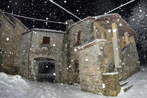 een oud steen huis terwijl sneeuwen in de winter nacht foto
