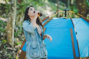 jong vrouw juichen en drinken drank voorkant van camping tent foto