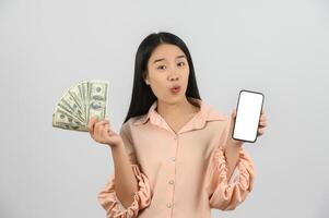 portret van een vrolijk jong vrouw Holding geld bankbiljetten en tonen smartphone mockup geïsoleerd over- wit achtergrond foto