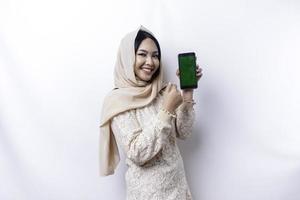 een portret van een gelukkig Aziatisch moslim vrouw vervelend een hijaab, tonen haar telefoon scherm, geïsoleerd door wit achtergrond foto