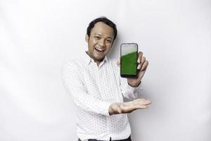 een portret van een glimlachen Aziatisch Mens vervelend een wit overhemd en tonen groen scherm Aan haar telefoon, geïsoleerd door wit achtergrond foto