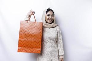portret Aziatisch moslim vrouw gelukkig mooi jong staand opgewonden Holding een boodschappen doen tas, studio schot geïsoleerd Aan wit achtergrond foto