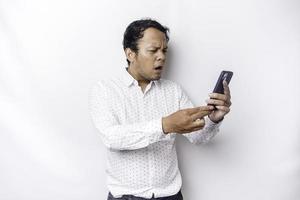 een boos jong Aziatisch Mens looks ontevreden vervelend een wit overhemd geërgerd gezicht uitdrukkingen Holding zijn telefoon foto