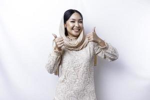 opgewonden Aziatisch moslim vrouw vervelend een hijab geeft duimen omhoog hand- gebaar van goedkeuring, geïsoleerd door wit achtergrond foto