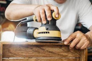 timmerman gebruikt excentrische schuurmachine of palmschuurmachine polijst hout in de werkplaats, doe-het-zelfmaker en houtbewerkingsconcept. selectieve focus foto