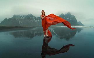 blootsvoets dame met rood kleding stof Aan reynisfjara strand toneel- fotografie foto