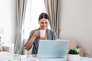 bedrijf Dames Bij huis gedurende pandemisch isolatie werken Aan laptop en drinken koffie.beeld van jong verheugd gelukkig vrolijk schattig mooi bedrijf vrouw zitten binnenshuis in kantoor gebruik makend van laptop computer foto