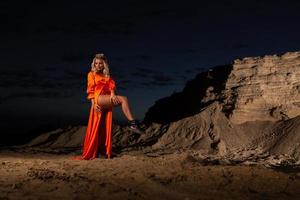 vrouw in oranje jurk met slank naakt poten poseren in de buurt de zand heuvel foto