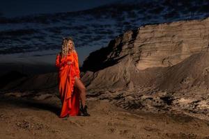 vrouw in oranje jurk met slank naakt poten poseren in de buurt de zand heuvel foto