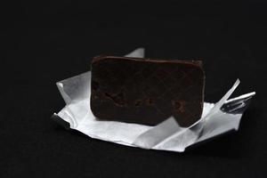chocola snoep in een pakket Aan een zwart achtergrond. zoet snoep. een chocola bar in een papier pakket. foto