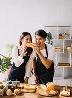 beeld van pasgetrouwde paar Koken Bij huis. Azië jong paar Koken samen met brood en fruit in knus keuken in huis foto