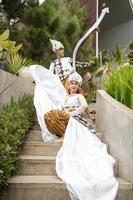 een paar van bruiden in wit kleren waren zittend Aan de trap met een vrolijk gezichten en vol van genegenheid in de midden- van de tuin foto