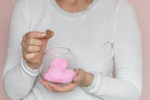 een vrouw houdt een transparant glas pot met een gebreid hart binnen, en zet een munt in haar andere hand. de concept van liefde, liefdadigheid en helpen. foto