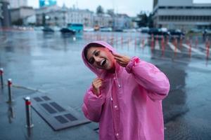 jong glimlachen vrouw in een roze regenjas genieten van een regenachtig dag. foto