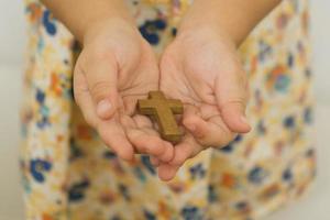 de handen van een kind met een houten christelijk kruis foto