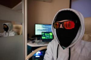 dichtbij omhoog van jongen hacker. internet diefstal . Mens vervelend een bivakmuts en zonnebril za achter een laptop. foto
