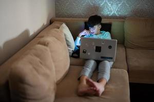 jong tiener jongen in voorkant van een laptop Aan een bed Bij avond. foto