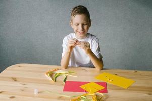 schattig jongen maakt een kaart door filigraan terwijl zittend Bij de tafel foto