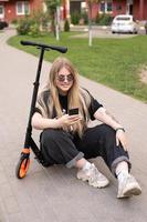 een tiener- meisje in zonnebril duurt een selfie Aan een scooter foto