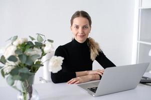 de meisje werken in een wit kantoor met een laptop en bloemen Aan de tafel foto