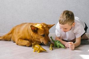 schattig jongen zit Aan de verdieping in de buurt zijn hond Bij huis en Toneelstukken met speelgoed foto