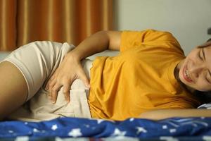 Aziatisch vrouw Aan de bed buik pijn van menstruatie foto