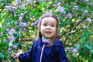 portret van schattig weinig meisje in een tuin met lila bomen. openhartig kind portret Bij voorjaar seizoen. foto