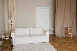 Scandinavisch interieur met een licht sofa Aan een houten parket vloer, een houten kant tafel en beige muren foto