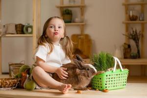 schattig weinig meisje in de houten keuken van de huis feeds de konijn vers gras foto