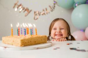 schattig weinig meisje slagen uit kaarsen Aan een verjaardag taart Bij huis tegen een backdrop van ballonnen. kind verjaardag