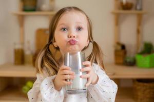 een schattig weinig meisje drankjes melk Bij huis in een houten keuken. melk dag foto