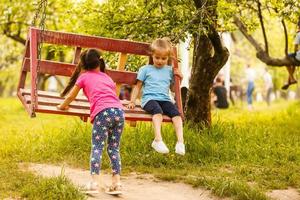 glimlachen weinig meisje Aan een schommel. kinderen spelen buitenshuis in zomer foto