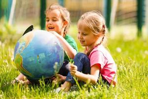 concept - onderwijs. terug naar school. twee vrolijk Kaukasisch meisjes schoolmeisjes met een wereldbol, gelukkig naar worden terugkeren huis na klasse in klasse foto