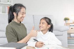 Aziatisch jong weinig meisje leren Bij huis. Doen huiswerk met soort moeder helpen, aanmoedigen voor examen. mam voorbij gaan aan Aan een glas van melk naar dochter. meisje gelukkig thuisschool. mam onderwijzen en advies onderwijs samen. foto