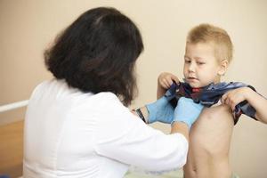 de dokter toepassingen een stethoscoop Aan de jongens maag naar controleren zijn Gezondheid. foto