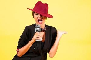 meisje in een zwart pak Aan een geel achtergrond zingt in een retro microfoon, portret, muziek- foto