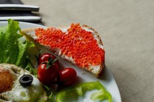 ontbijt, door elkaar gegooid eieren Aan sla bladeren, De volgende naar vers groenten en een belegd broodje met rood kaviaar foto