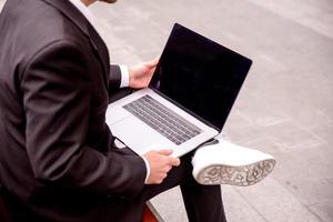 jong vent in een pak werken Aan een computer in de park, laptop dichtbij omhoog foto