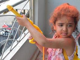 zoet weinig Indisch meisje spelen kleuren Aan holi festival, Holding pichakaree vol van kleuren, holi festival vieringen in Delhi, Indië foto