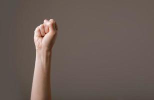 vrouwelijke hand gebald in een vuist op een grijze achtergrond. gebaar van vechten, winnen of protesteren. menselijke hand gebaren teken geïsoleerd. vrouwelijke opgeheven arm die populair gebaar voorstelt. kopieer ruimte foto