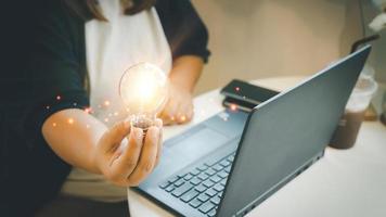 zakenvrouw hand- Holding gloeilamp met een notitieboekje computer in een koffie winkel. idee, innovatie inspiratie concept. foto