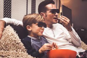 klein jongen en zijn vader aan het kijken film met 3d bril en aan het eten popcorn. foto