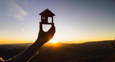 silhouet van vrouw handen Holding model- huis Bij zonsondergang concept van buying huizen, echt landgoed. foto