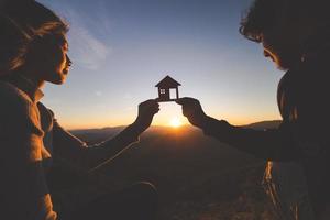 silhouet van mannetje en vrouw handen Holding model- huis Bij zonsondergang concept van buying huizen, echt landgoed. foto