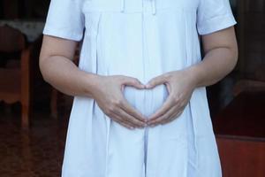 detailopname 6 maand pragnant vrouw draagt wit jurk, handen tintje haar groot buik. concept, zwangerschap, moederschap. Gezondheid zorg. foto