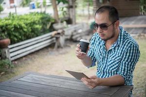 jonge man zit buiten aan een houten tafel en ontspannen met tablet foto