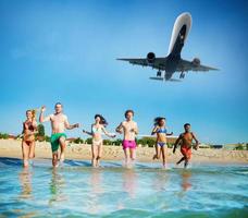 groep van vrienden rennen in de zee met vliegtuig in de lucht. concept van zomertijd foto