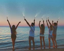 gelukkig glimlachen vrienden Bij de strand met sprankelend kaarsen foto