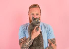 Mens met baard en tatoeages liefkozingen een grijs kat foto